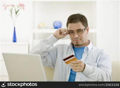Casual man at home using laptop computer purchasing by credit card.