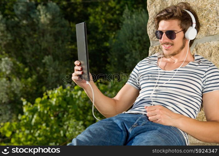 casual man holding a tablet with headphones, outdoor