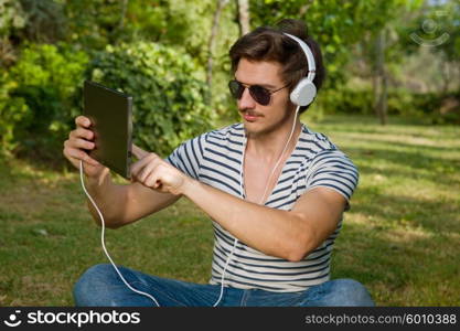 casual man holding a tablet with headphones, outdoor