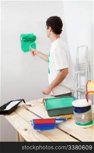Casual man painting the wall of his new apartment with paint bucket in background