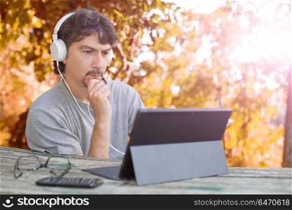 casual man working with a tablet pc, with headphones, outdoor. working