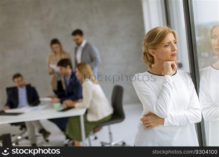 Casual mature business woman standing in the office in front of her team