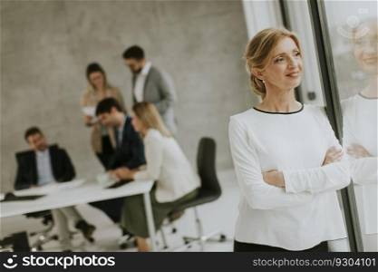 Casual mature business woman standing in the office in front of her team