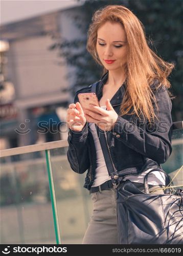 Casual modern young woman checking her social media, using smartphone outdoor. Fashionable female wearing jeans jacket with phone.. Fashionable woman using phone outdoor