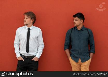 Casual multiethnic startup businessmen during a break from work in front of the red wall outside. High-quality photo. Casual multiethnic startup business men during break from work in front of red wall outside