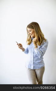 Casual pretty  young  business woman standing by the wall in the office and using mobile phone