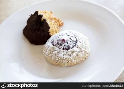 Casual snack of powdered Linzer cookie placed with coconut macaroon dipped in chocolate on white plate on marble table. One is a classic Austrian dessert and the other is a traditional French sweet.