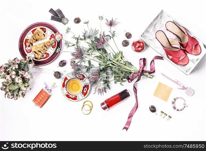 Casual woman beauty blog flat lay composition. Red high heels in box, cosmetics, perfume, flowers bunch, cakes cup of tea and bijou on white desk background. Top view. Fashion blogging template