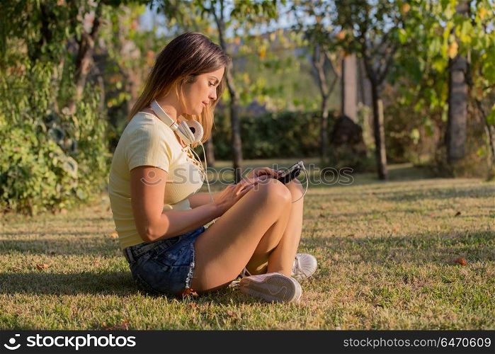 casual woman working with a tablet pc, with headphones, outdoor. woman with tablet
