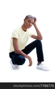 Casual young African man in yellow shirt and jeans squatting and worried, isolated