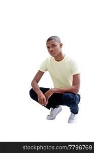 Casual young African man in yellow shirt and jeans squatting, isolated