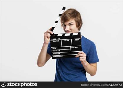Casual young man holding a clapboard, over a gray background