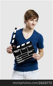 Casual young man holding a clapboard, over a gray background