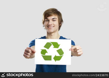 Casual young man holding a recycling sign to promote a green and better world, over a gray background
