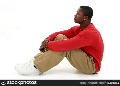 Casual young man in red long sleeve shirt sitting on white backdrop thinking. Full body