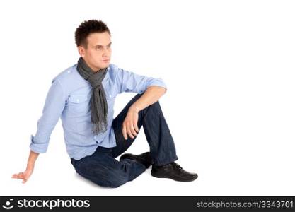 Casual young man in shirt and jeans sitting on the ground, isolated on white background, copyspace on right side.