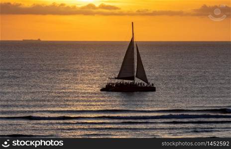 Catamaran sailing at sunset with beautiful orange sky behind it