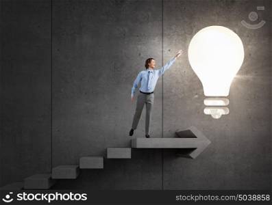 Catch bright idea. Young businessman on ladder reaching hand to touch glowing light bulb