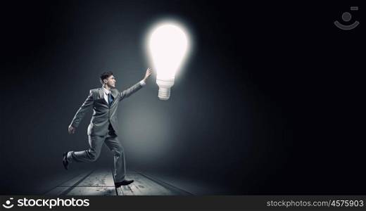 Catch bright idea. Young businessman running and catching glowing light bulb