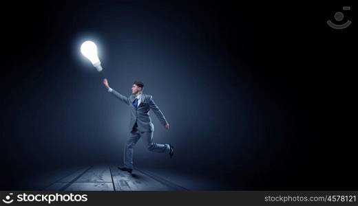 Catch bright idea. Young businessman running and catching glowing light bulb
