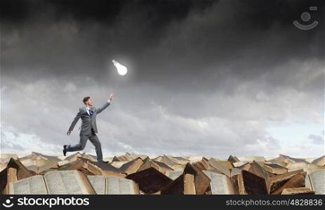Catch your bright idea. Running young businessman trying to catch glowing light bulb