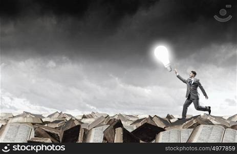 Catch your bright idea. Running young businessman trying to catch glowing light bulb