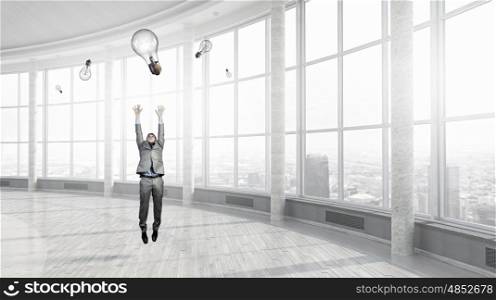 Catch your bright idea. Young businessman in modern interior jumping to catch idea bulb