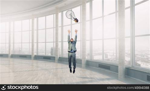 Catch your bright idea. Young businessman in modern interior jumping to catch idea bulb