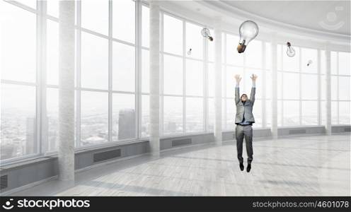 Catch your bright idea. Young businessman jumping and catching light bulb