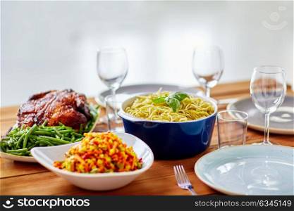 catering and eating concept - pasta with basil in bowl and other food on wooden table. pasta with basil in bowl and other food on table