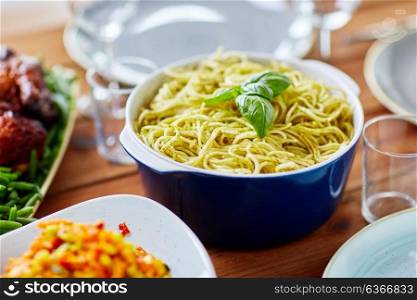 catering and eating concept - pasta with basil in bowl and other food on wooden table. pasta with basil in bowl and other food on table