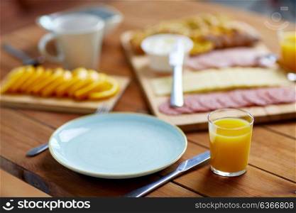 catering and eating concept - plate and glass of orange juice on wooden table with food. plate and glass of orange juice on table with food