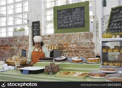 Catering assistant stands in service area of canteen