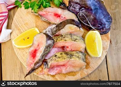 Catfish raw sliced pieces on a circular board, parsley, lemon, napkin on a wooden boards background