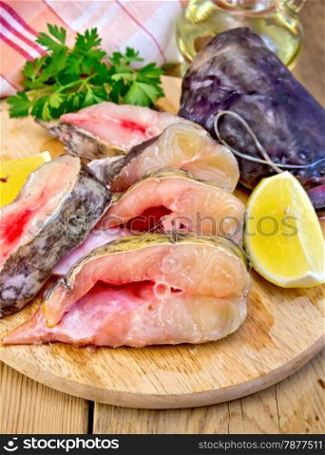 Catfish raw sliced pieces on a circular board, parsley, lemon, oil, cloth on a wooden boards background