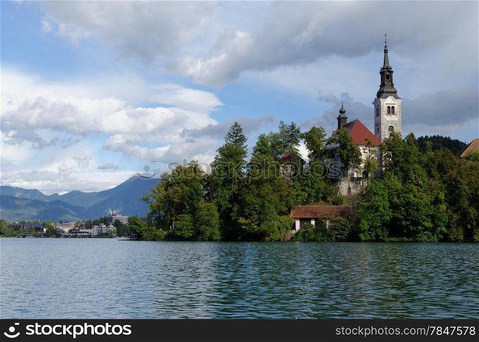 Catholic church situated on an island on Bled lake with mountains and resort on the background