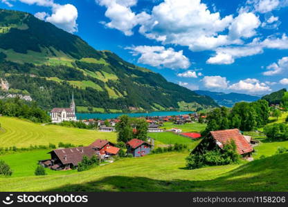 Catholic church, traditional wood and modern houses along the lake Lungernsee in swiss village Lungern in sunny summer day, Obwalden, Switzerland. Swiss village Lungern, Switzerland