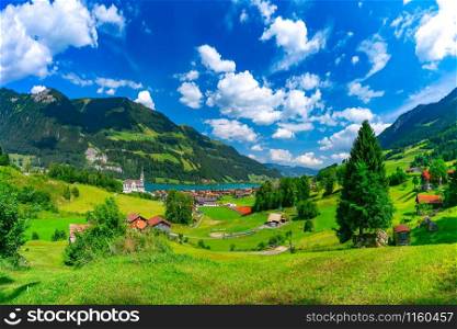 Catholic church, traditional wood and modern houses along the lake Lungernsee in swiss village Lungern in sunny summer day, Obwalden, Switzerland. Swiss village Lungern, Switzerland