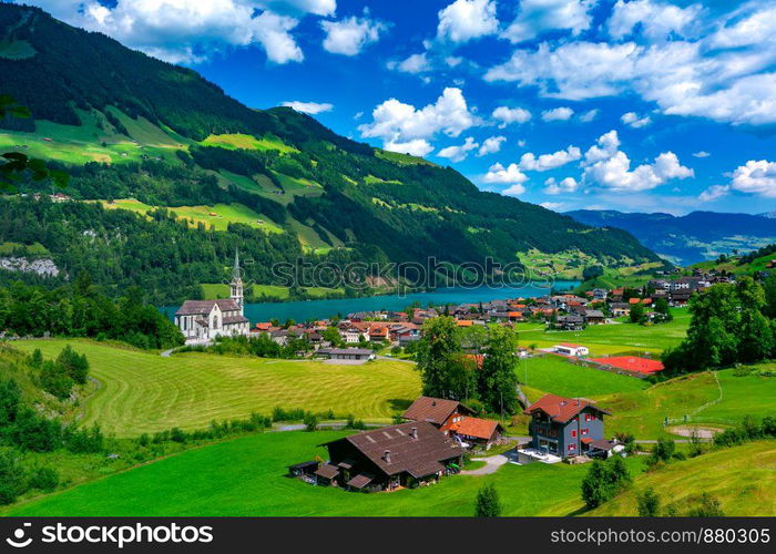 Catholic church, traditional wood and modern houses along the lake Lungernsee in swiss village Lungern, canton of Obwalden, Switzerland. Swiss village Lungern, Switzerland