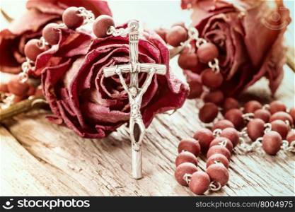 Catholic rosary and dry roses on old wooden background