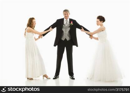 Caucasian and Asian brides pulling on Caucasian groom&acute;s arms.