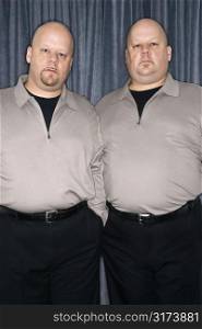 Caucasian bald identical twin mid adult men standing together looking at viewer.