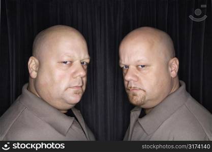 Caucasian bald mid adult identical twin men looking sternly at viewer.