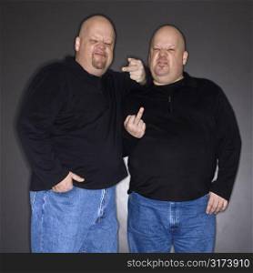 Caucasian bald mid adult identical twin men making obscene gesture at viewer.