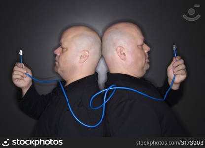 Caucasian bald mid adult identical twin men standing back to back holding ethernet cable.