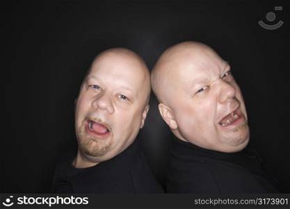 Caucasian bald mid adult identical twin men standing back to back with sad expressions looking at viewer.