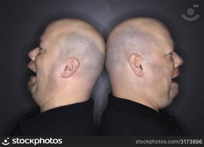 Caucasian bald mid adult identical twin men standing back to back with sad expressions.