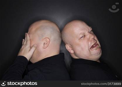 Caucasian bald mid adult identical twin men standing back to back with sad expressions.