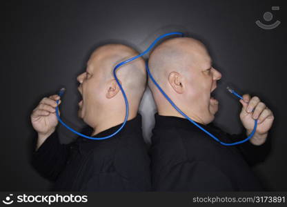 Caucasian bald mid adult identical twin men standing back to back yelling into ethernet cable.