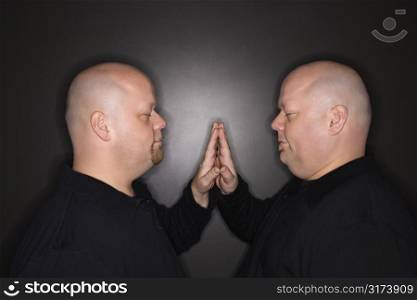 Caucasian bald mid adult identical twin men standing face to face with hands touching.
